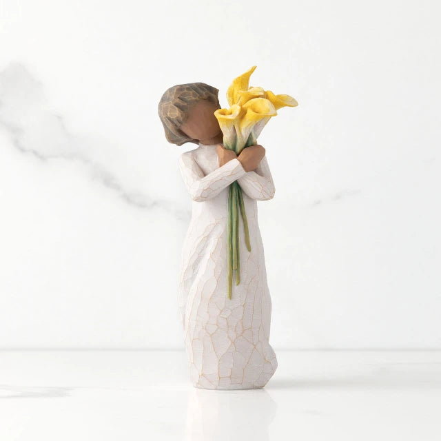 Willow Tree® Front view of standing figure in cream dress with darker skin holding yellow calla lilies in her arms