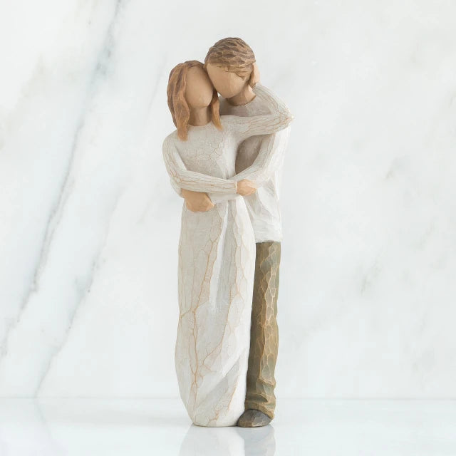 Willow Tree® Faceless man and woman figurines with arms around each other - woman is wearing white dress, man is wearing white shirt with brown pants