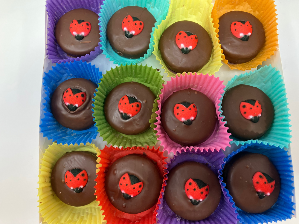 Chocolate candies with ladybug designs in colorful paper cups on a white background