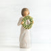 Willow Tree® Front view of young girl with bangs and short brown hair holding up a green, leafy wreath