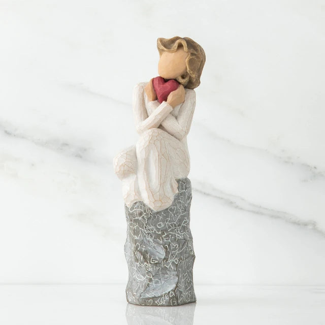 Willow Tree® Young faceless little girl sitting on silver rock - she is wearing white and holding pink heart