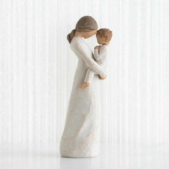 Willow Tree® Side view of faceless mom figurine wearing white dress holding child in white outfit in her arms