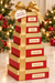 Bear Creek Candy Kitchen six-box red-and-gold holiday gift tower with a gold bow; boxes labeled chocolate truffles, sea-salt caramels, peanut brittle, pecan pralines, pecan turtles, and chocolate fudge.