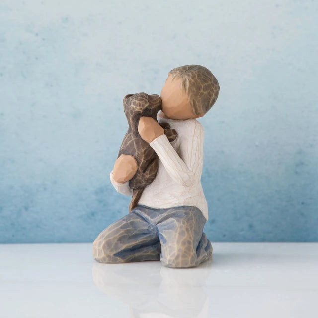 Willow Tree® Young faceless boy figurine wearing white shirt and blue jeans sitting holding brown puppy - background is blue