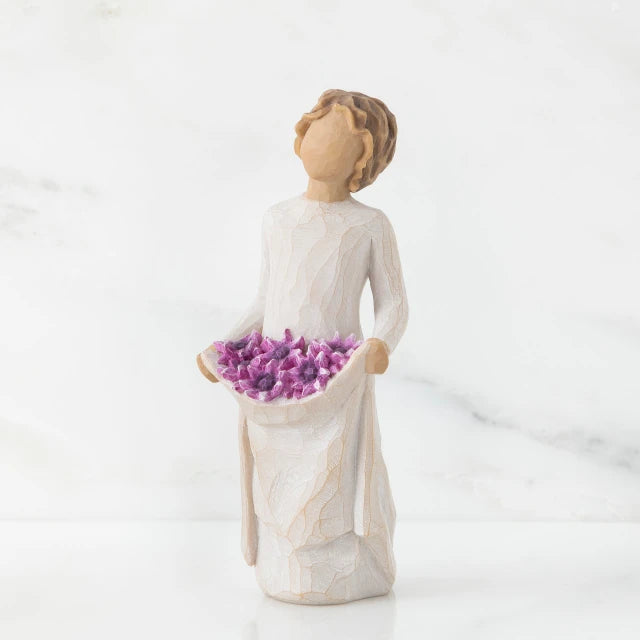 Willow Tree® Front view of woman with tied back, curly, light brown hair holds up a portion of her dress's skirt as it is full of purple flowers