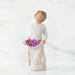 Willow Tree® Front view of woman with tied back, curly, light brown hair holds up a portion of her dress's skirt as it is full of purple flowers