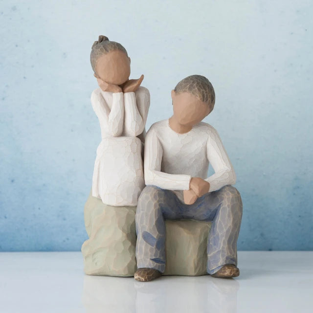 Willow Tree® Young girl faceless figurine sitting on rock next to young faceless boy figurine wearing white shirt and blue jeans