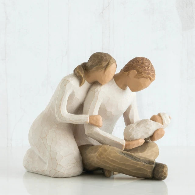 Willow Tree® Faceless woman figurine in white dress leaning on faceless man figurine holding baby in his lap