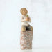 Willow Tree® Front view of boy with brown hair sitting on a stump while holding a small potted plant to his chest