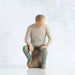 Willow Tree® Front view, adult male figure in light gray shirt and blue jeans, seated on gray rock