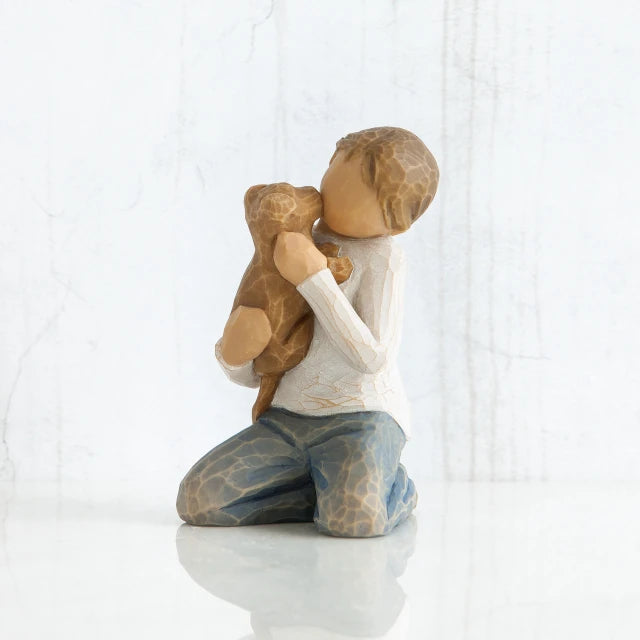 Willow Tree® Front view of boy with iight brown hair wearing white shirt and jeans and holding a light brown puppy as it licks his face.