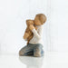 Willow Tree® Front view of boy with iight brown hair wearing white shirt and jeans and holding a light brown puppy as it licks his face.