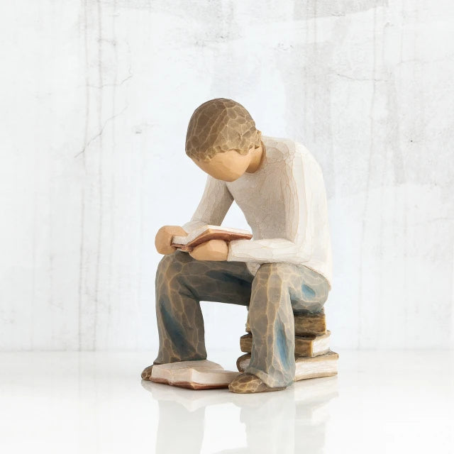 Willow Tree® Young faceless boy figurine sitting on books with book opened in his hands - another book on the floor of his feet