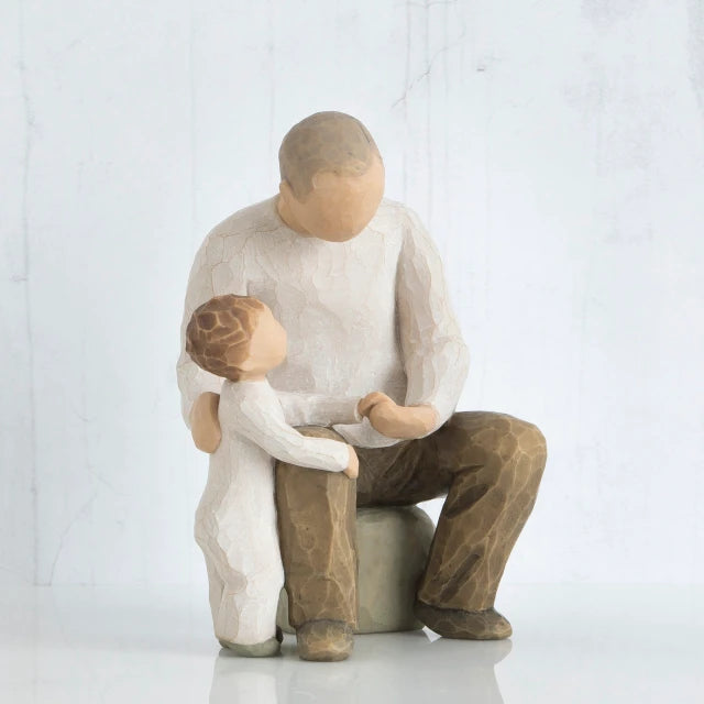 Willow Tree® Faceless dad figurine sitting on rock holding little boy figurine's hand