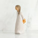 Willow Tree® Right side view of girl with brown hair in braid over right shoulder leaning forward as she holds orange flowers behind her back