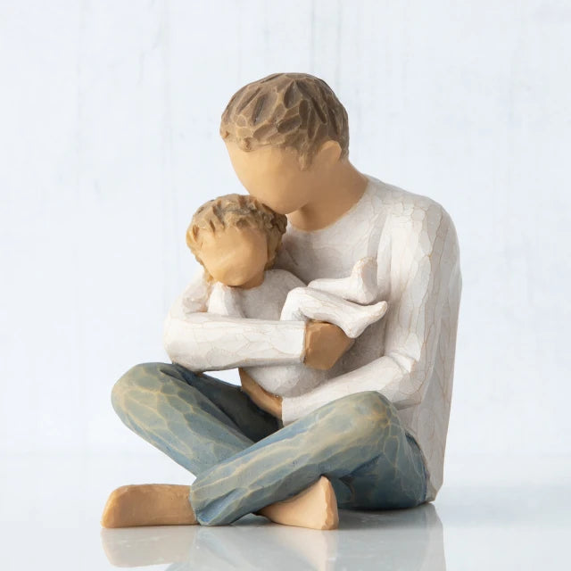Willow Tree® Front view, seated male figure in cream shirt and blue jeans, holding young child in his arms; child in cream onesie