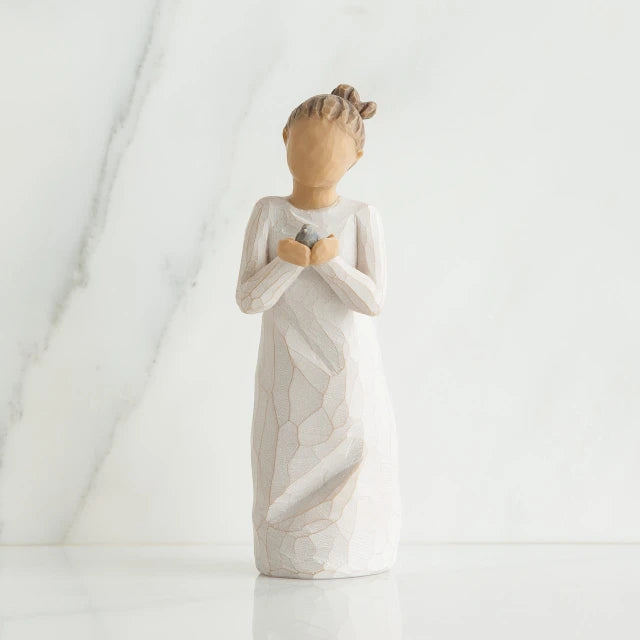 Willow Tree® Front view of woman with brown hair in a high ponytail leans forward as she holds a gray bird to her chest with both hands