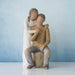 Willow Tree® Man figurine sitting on rock wearing brown shirt and blue jeans with woman figurine in white dress with arms wrapped around him - blue background