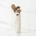 Willow Tree® Front view, standing female figure in cream dress, holding dark color puppy in her arms