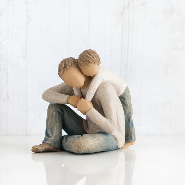 Willow Tree® Faceless man figurine sitting with young boy hugging him over his shoulders - wearing white shirts and blue jeans - all white background