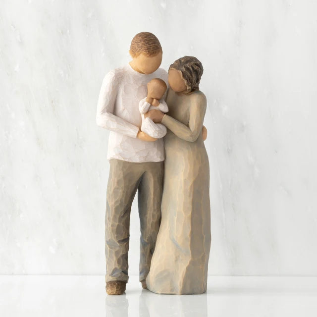 Willow Tree® Front view of standing couple, woman has darker skin and hair; man has lighter skin and hair, holding a baby between them.