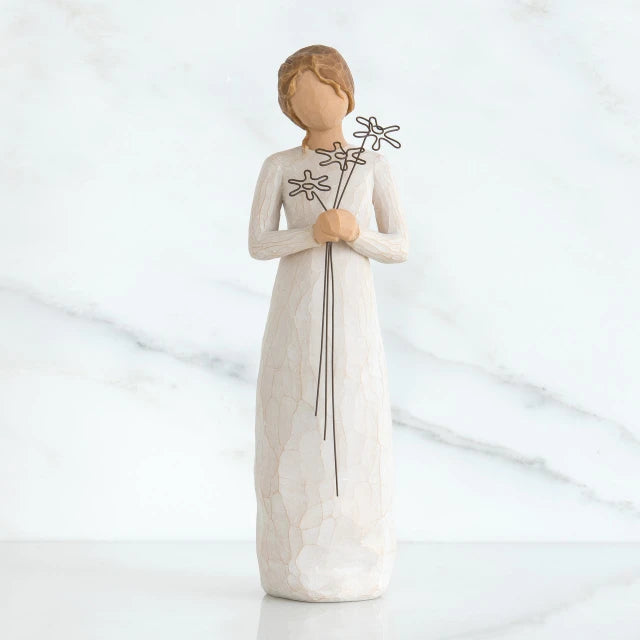 Willow Tree® Front view of girl with brown hair in a bun holding three flowers with long stems up to her chest with both hands