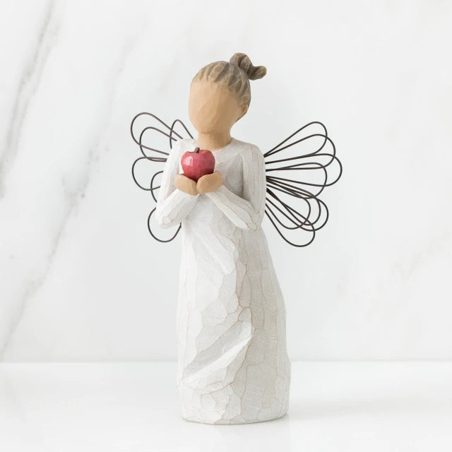 Willow Tree® Front view of angel with brown hair in high pony tail leaning forward and holding a red apple up to her face with both hands