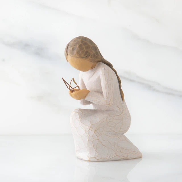 Willow Tree® Side view of kneeling female figure in cream dress, with wire butterfly on extended hands, on marble background