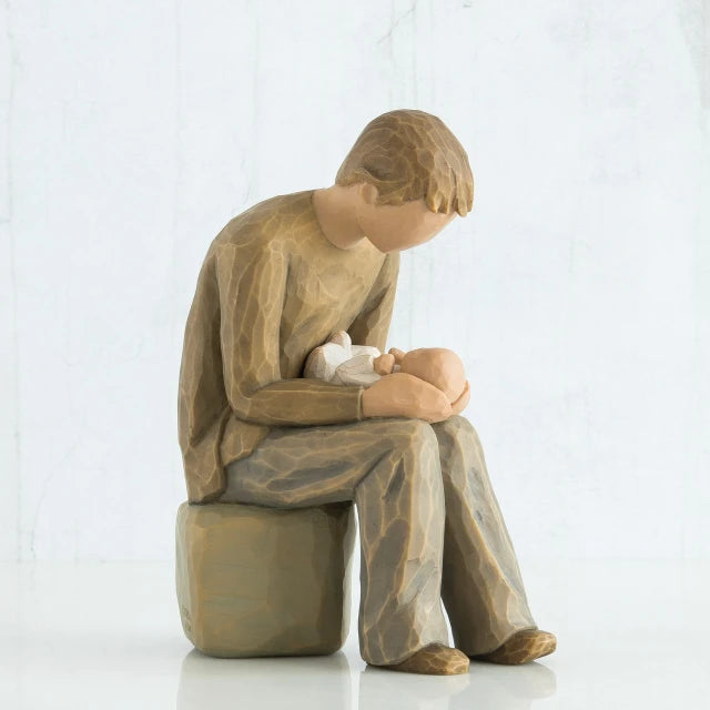 Willow Tree® Man faceless figurine dressed in light brown sitting on rock holding baby in arms