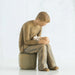 Willow Tree® Man faceless figurine dressed in light brown sitting on rock holding baby in arms