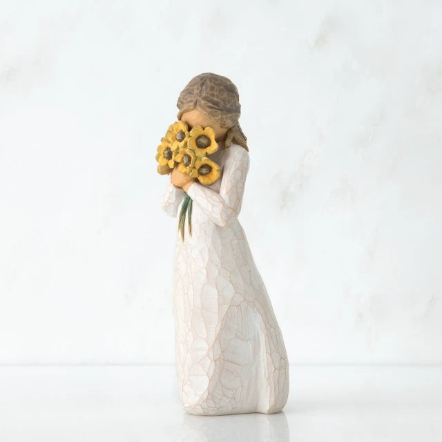 Willow Tree® Side view of woman with tied back brown hair holding a cluster of yellow flowers to her face