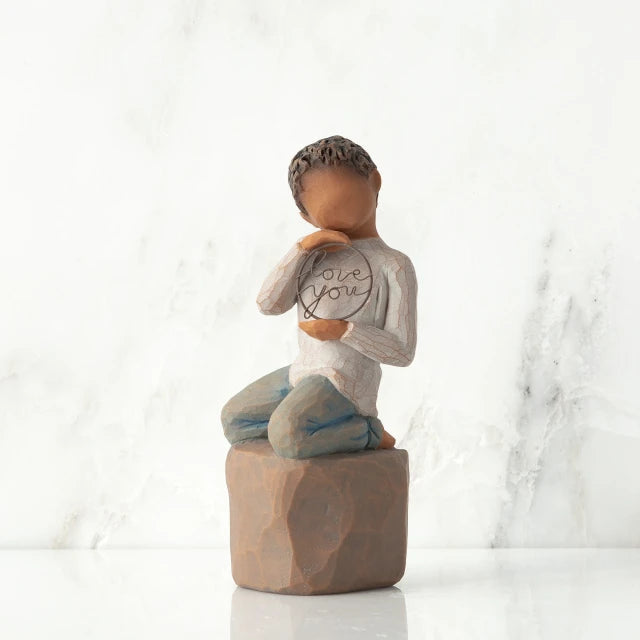 Willow Tree® Front view: Figure of darker-skin child, kneeling on rock, holding wire circle with ‘love you’ written in wire