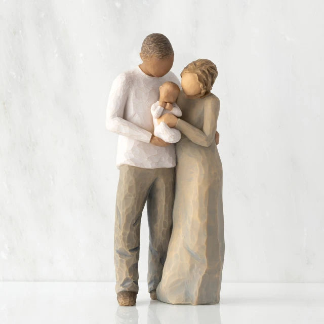 Willow Tree® Front view of standing couple, woman has lighter skin and hair; man has darker skin and hair, holding a baby between them.